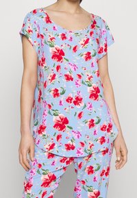 Top con stampa floreale, scollo a barca, maniche corte e orlo curvo, realizzato in tessuto leggero nelle tonalità di blu, rosso e verde.