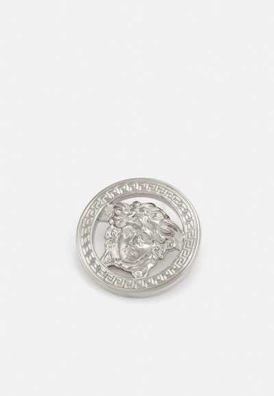 Médaille ronde en argent présentant un motif en relief d'un visage ayant des cheveux ondulés, entouré d'un motif clé grec le long du bord.