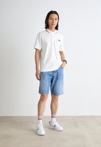 White polo shirt with red collar accents, denim shorts, white sneakers with green details, and striped socks. Simple, casual design.
