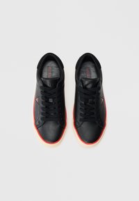 Μαύρα δερμάτινα αθλητικά παπούτσια με κόκκινα στοιχεία, στρογγυλεμένη μύτη και μαύρα κορδόνια. Διαθέτουν υφή στη σόλα και λογότυπο στην εσωτερική σόλα.