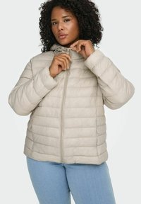 Bēšs pūkains džemperis ar horizontālu šūšanas dizainu, priekšējā rāvējslēdzēja aizdare un kapuce ar auklu. Mīksta tekstūra un brīvs fitējums, valkāts kopā ar gaišiem džinsiem.