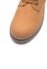 Brūns ādas šņorējams apavs ar noapaļotu purngalu, kontrastējošiem baltajiem diegiem un teksturētu gumijas zoli. Uzsvars uz elegantu, minimālistisku dizainu.