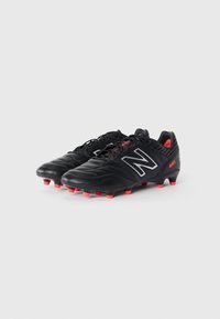 Baskets de football noires avec tige en cuir texturé, logo argenté et accents rouges sur la semelle. Équipées d'un système de laçage traditionnel et de crampons coniques.