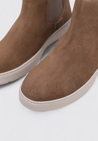 Bottes de cheville en daim marron avec une finition lisse, semelle en caoutchouc blanc contrasté, panneaux latéraux en élasthanne et détail de couture minimaliste.