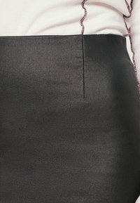 Zwarte kokerrok met een gladde, glanzende textuur en een subtiel naaddetail. Gecombineerd met een wit topje versierd met een golvende paarse omlijning.