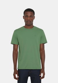 T-shirt verde a maniche corte realizzato in materiale morbido con scollatura rotonda, caratterizzato da un logo discreto dello stesso colore sul petto.