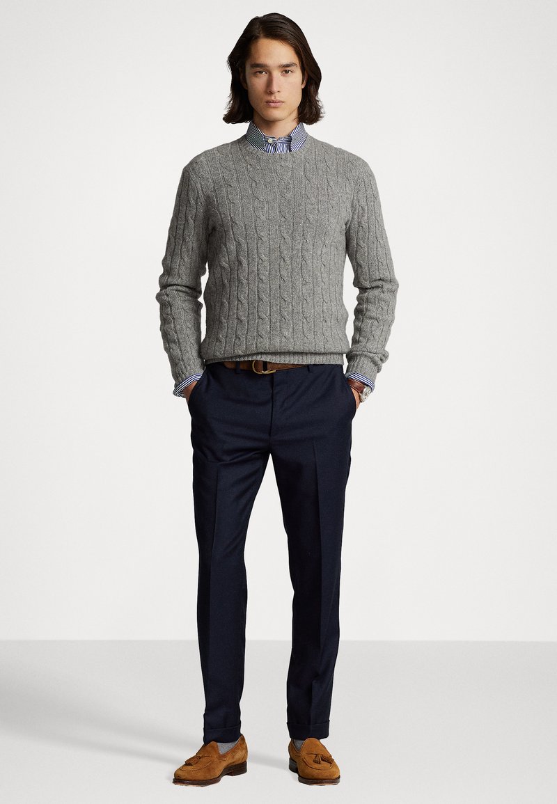 Un pull en maille gris sur une chemise à rayures bleues et blanches, associé à un pantalon sombre et des mocassins marron.