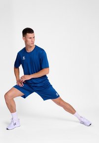 Tenue de sport bleue composée d'un t-shirt à manches courtes et d'un short, fabriquée à partir d'un tissu respirant, assortie de chaussures et de chaussettes de sport blanches.