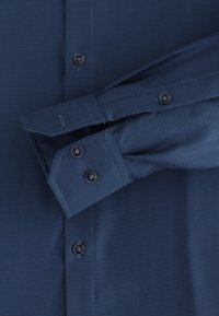 Dunkelblaues Hemd mit einem strukturierten Muster. Es verfügt über einen Spitzkragen, Knopfmanschetten und schwarze Knöpfe und zeigt ein maßgeschneidertes Design.