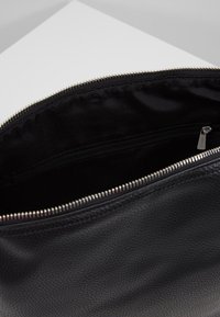 Svart läderväska med texturerad yta, utrustad med ett mjukt dragkedjestängning och ett svart tygfoder med en inre ficka.