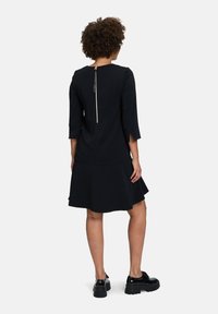 Schwarzes Kleid mit Dreiviertelärmeln, tailliertem Oberteil, ausgestelltem Rock und einem auffälligen Reißverschlussdetail am Rücken. Glatter Stoff und kniebedeckendes Design.