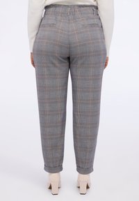 Pantalones de cuadros grises con cinturilla elástica, que cuentan con bolsillos y dobladillos con puños. Combinados con zapatos de tacón bloque beige.