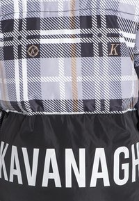 Kurtka pikowana w szaro-czarnym-białym kratkowanym wzorze, z złotymi akcentami oraz czarną dolną częścią z dużymi białymi literami "KAVANAGH".