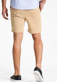 Shorts beiges à coupe droite, avec un ourlet plié et en doux coton, assortis à des baskets noires avec une semelle blanche.