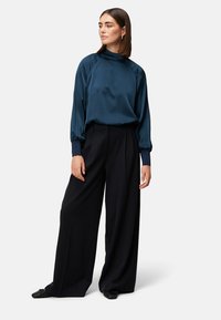 Seidige, tiefblaue Bluse mit hohem Kragen und puffigen Ärmeln, kombiniert mit weit geschnittenen schwarzen Hosen. Glatte Textur mit sanftem Fall.