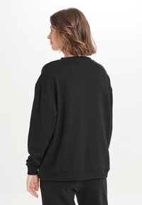 Zwarte oversized sweatshirt met een ronde hals, geribbelde manchetten en een relaxte pasvorm. Het materiaal lijkt zacht met een gladde textuur, zonder zichtbare patronen.