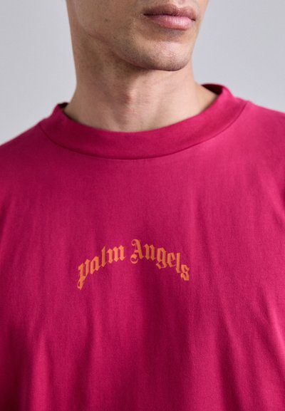 Fuchsia bomulds t-shirt med rund hals og teksten "palm Angels" i guld skrift på brystet. Glat tekstur.