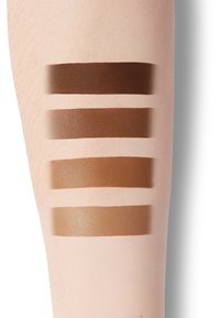 Swatches of five foundation shades in varying brown tones on a light skin arm, with smooth texture and rich, matte finishes.