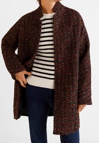 Abrigo de punto en una tela texturada oscura con motas multicolores, con un cuello mao y cierre de botones, superpuesto a un suéter a rayas.