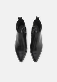 Botas de tornozelo em couro preto com bico fino, textura suave, fecho lateral e alça para facilitar o calçar. Nome da marca por dentro.
