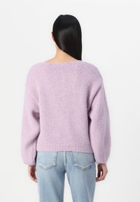Pulover tricotat de culoare liliachiu, cu croi lejer, umeri lăsați și tiv cu nervuri. Textură moale, mâneci largi și design cu spatele deschis.