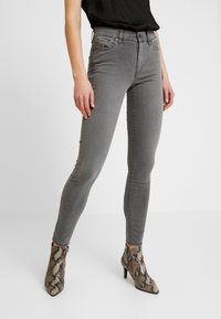Jeans ajustados gris con bolsillos delanteros, cierre de botones y trabillas para cinturón, combinados con botines de tacón con estampado de serpiente. Textura suave de mezclilla.