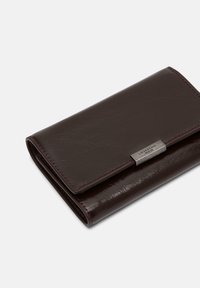 Ciemnobrązowy portfel ze skóry o gładkiej fakturze, z klapką i srebrnym metalowym akcentem na przodzie.