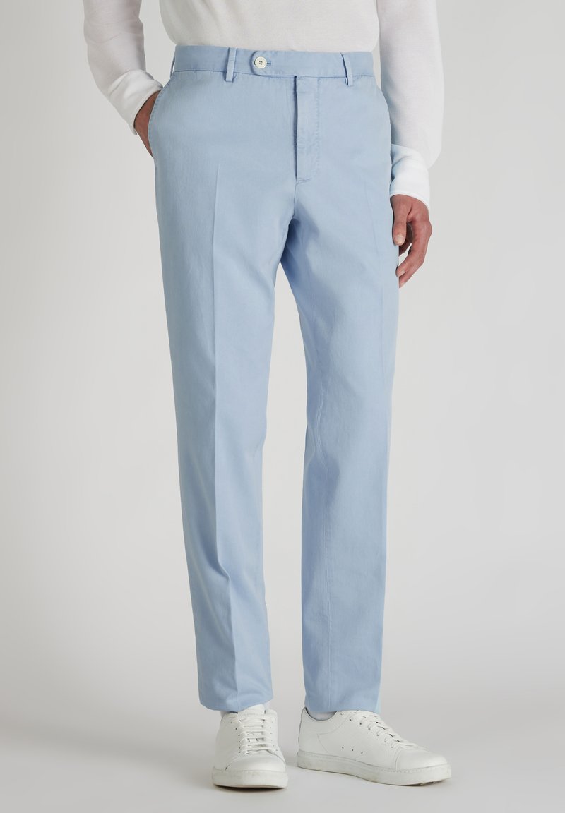 Jasnoniebieskie bawełniane spodnie z płaskim przodem, kieszeniami po bokach i zapięciem na guzik. W połączeniu z białymi trampkami, co podkreśla swobodny styl.