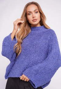 Purple textured sweater with a high neckline and wide sleeves, featuring a cozy, loose fit. The fabric appears soft and chunky.