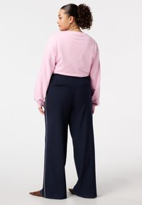 Lichtroze langemouwen top met een ronde hals, gecombineerd met marineblauwe wijde broek met zijstripes en een geribde textuur.