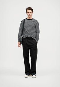 Fekete és fehér csíkos hosszú ujjú ing, fekete nadrággal párosítva. Tengerészkék sportcipőt és fekete válltáskát visel.