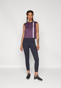 Μωβ αμάνικο κοντό τοπ με μια λευκή ρίγα, σε συνδυασμό με μαύρα κολάν. Διαθέτει λεία υφή και αθλητική εφαρμογή. Μαύρα αθλητικά παπούτσια ολοκληρώνουν την εμφάνιση.