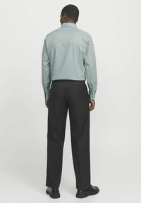 Lichtblauwe overhemd met lange mouwen en een kraag, gecombineerd met zwarte broek met achterzakken, gezien vanaf de achterkant.