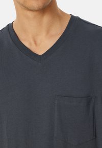 Dunkelgraues V-Ausschnitt-T-Shirt aus Baumwoll-Mischgewebe mit einer quadratischen Fronttasche, glatter Textur und dezenten Nahtdetails.