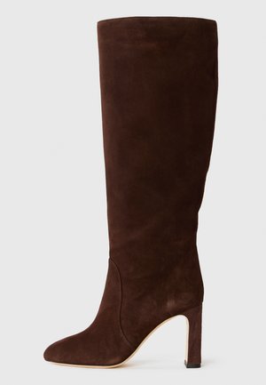 Braune Wildleder-Stiefel bis zum Knie mit einer spitzen Zehe und geometrischem Blockabsatz, die eine glatte Textur und klare Linien aufweisen.