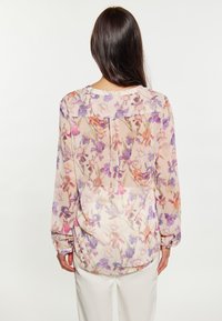 Durchsichtige Bluse mit floralem Muster in Lila, Pink und Cremefarben. Mit langen Ärmeln und abgerundetem Saum. Leichter und fließender Stoff.