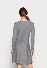 Robe-pull grise avec des manches longues et un col rond, présentant un haut ajusté et une jupe évasée. Texture tricot douce.