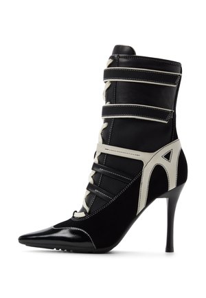 Sort ankelstøvle med høje hæle, spids tå, snørebånd foran, hvide og sorte remme samt hvide geometriske detaljer på siderne.