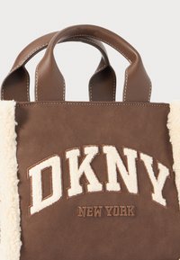 Brown leather tote bag with cream plush trim, featuring an embroidered "DKNY NEW YORK" logo in white and brown on the front.