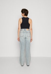 Top sin mangas negro de canalé combinado con jeans de pierna ancha de cintura alta en azul claro, que cuentan con un parche en la parte posterior y dos bolsillos traseros.