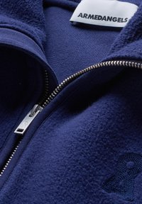 Marineblaue Jacke mit Reißverschluss, aus weichem, strukturiertem Stoff, mit Logodetail und metallischem Reißverschluss für einen sicheren Sitz.