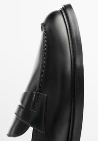 Scarpa in pelle nera con punta rotonda, caratterizzata da una cucitura prominente e una fascia decorativa sopra la tomaia. Suola piatta.