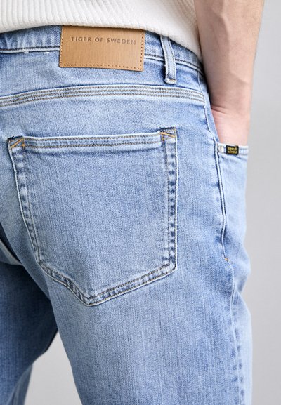 Lichtblauwe denim jeans met een leren label met "TIGER OF SWEDEN" aan de achterkant, met een standaard zakdesign en zichtbare stiksels.