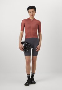Completo da ciclismo con una maglietta a maniche corte color ruggine, pantaloni grigi, caschetto nero e scarpe nere con dettagli vivaci.