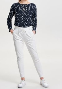 Långärmad marinblå topp med vitt hjärtmönster, i kombination med vita smala byxor och vita sneakers. En enkel, avslappnad outfitdesign.