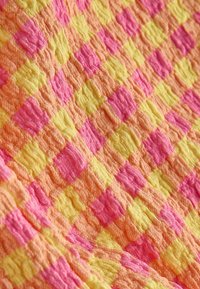 Tissu à texture douce avec un motif répétitif de carrés roses, orange et jaunes dans un design à grille froissée.