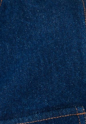 Primer plano de tela de mezclilla azul oscuro con textura visible de tejido diagonal y costuras contrastantes en color naranja.