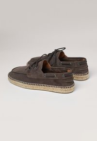 Zapatos de ante marrón tipo slip-on con interior de cuero en contraste en tono beige, cordones decorativos y suelas envueltas en yute. Incluye ojetes metálicos para los cordones.