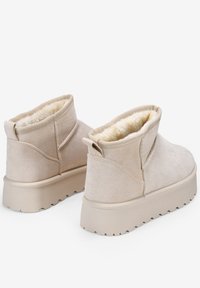 Botas de tobillo beige hechas de suave ante con un interior acolchado. Cuentan con una suela de goma gruesa y un diseño de punta redondeada para mayor comodidad.