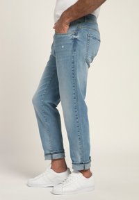 Vaqueros de denim azul claro con un corte relajado, que presentan un ligero desgastado, puños enrollados y un diseño de cinco bolsillos. Combinados con zapatillas blancas.